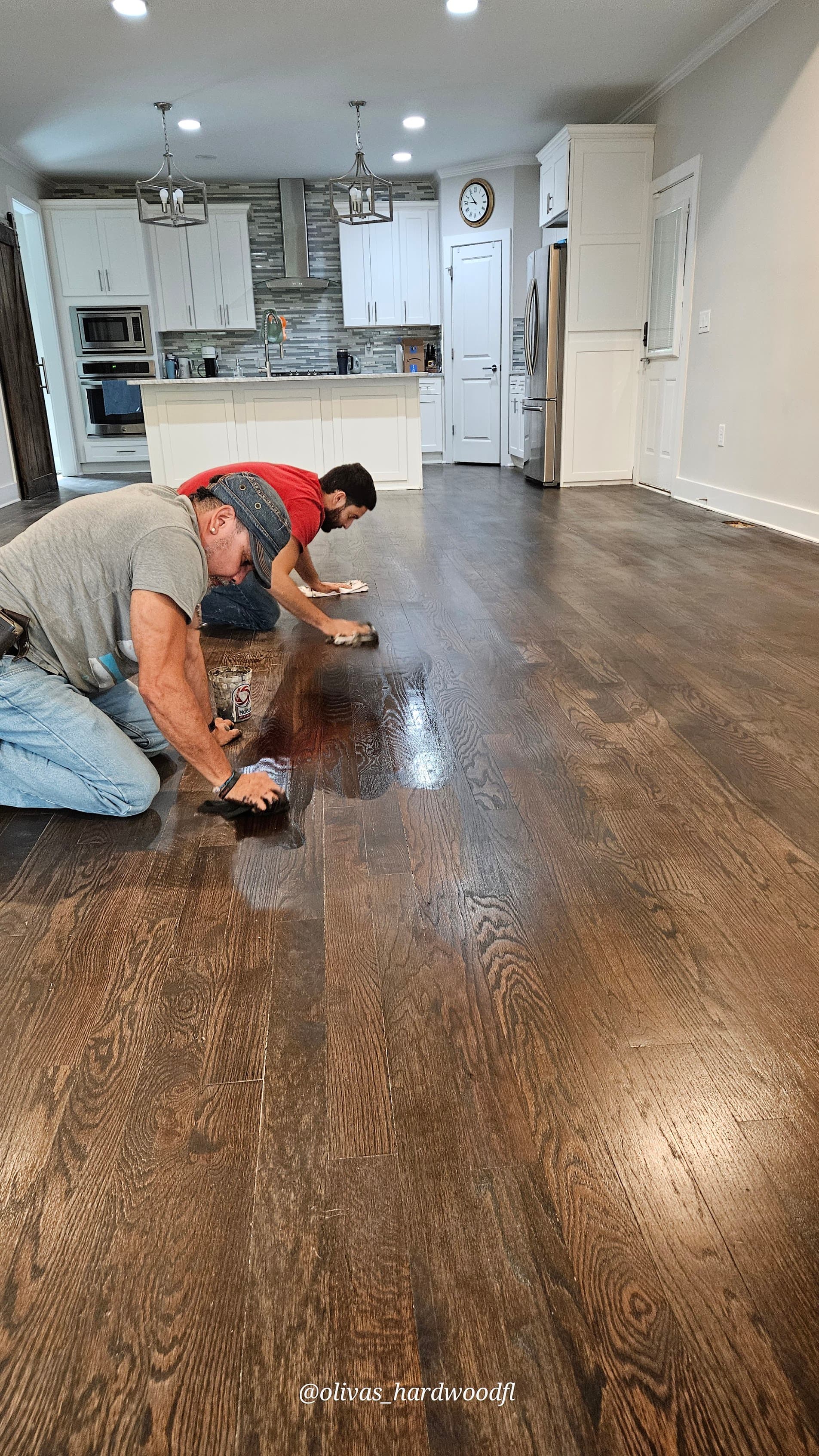 Crew applying dark stain to oak floor in an open-plan kitchen in Lawrenceville, GA