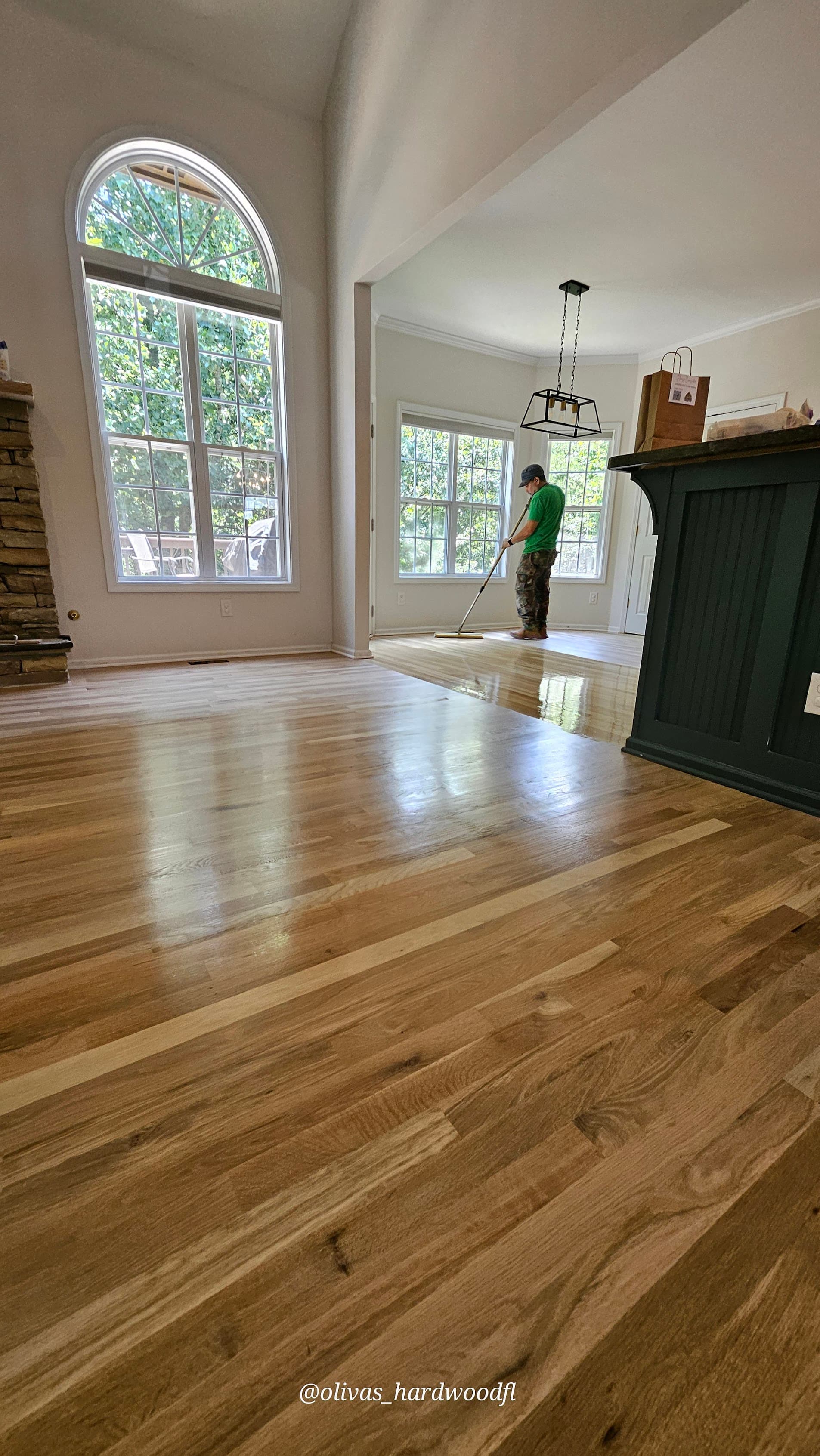Crew applying finish to natural oak living room floor with stone fireplace in Gwinnett County, GA