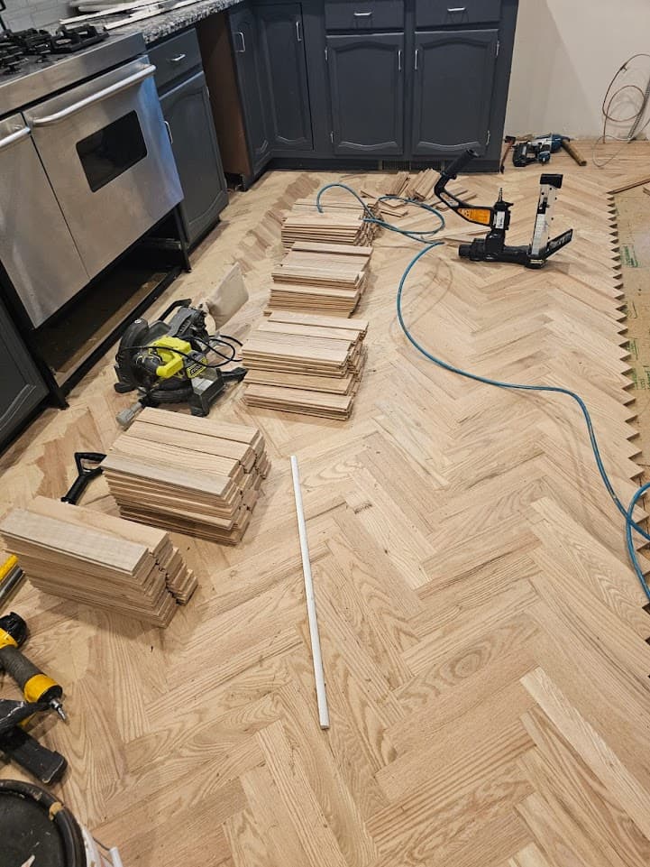 Herringbone hardwood floor installation in Marietta GA — red oak parquet being cut and nailed in kitchen